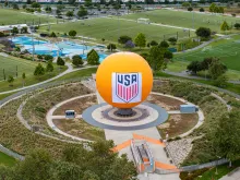 Large orange sphere with USA logo in a circular park, surrounded by green sports fields.