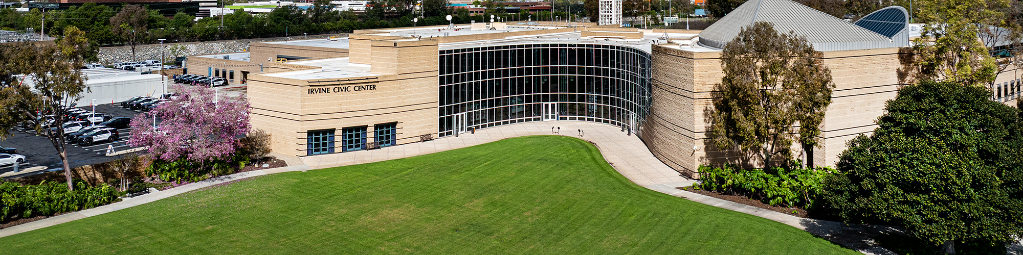 Irvine City Hall, a Modern tan building with large glass entrance, green lawn, and trees under a blue sky.