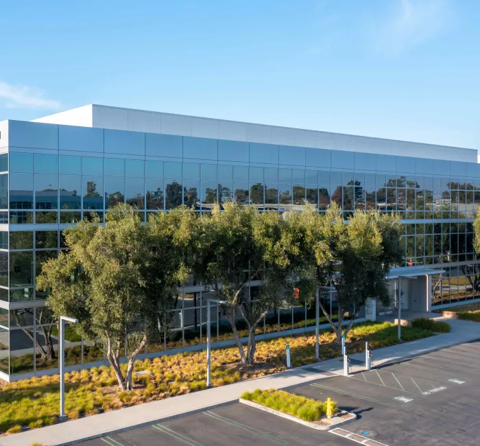 Modern glass office building with trees and landscaping under a blue sky.