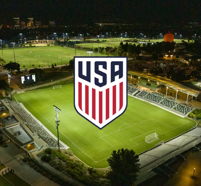 USA soccer logo over a brightly lit stadium at night, with city lights in background.
