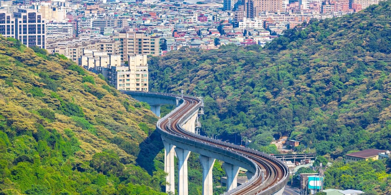 Photograph: Elevated train tracks curve through green hills towards a city skyline.
