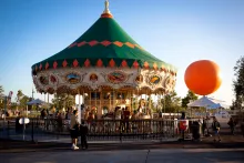 Amusement park carousel with green roof and a large orange balloon.