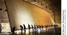 Photograph of workers collaboratively unrolling an enormous beige fabric in a vast hangar.