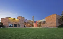 Modern Irvine Civic Center with glass facade, clock tower, and American flag over green lawn.