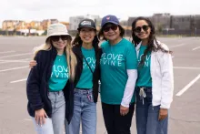 Four smiling women in teal "LOVE IRVINE" shirts stand in a parking lot.