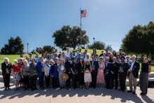 Large group of people holding awards under an American flag on a sunny day.