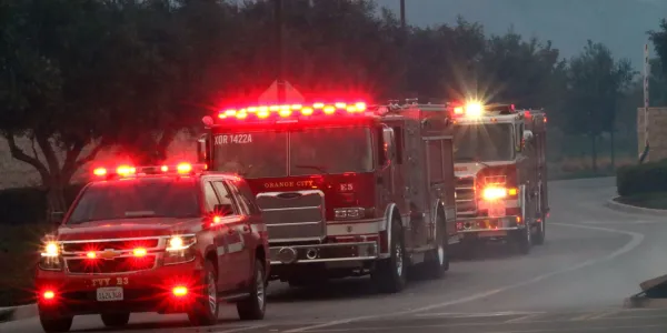 A line of fire trucks with flashing red lights on a road at dusk.