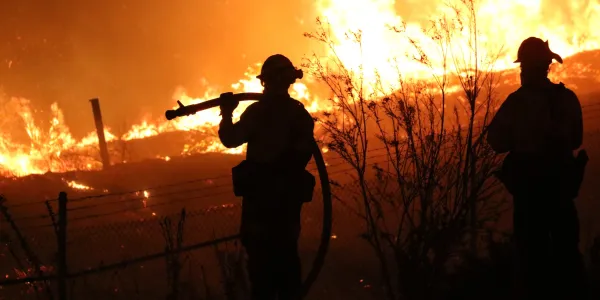 Silhouetted firefighters watching a raging wildfire at night.
