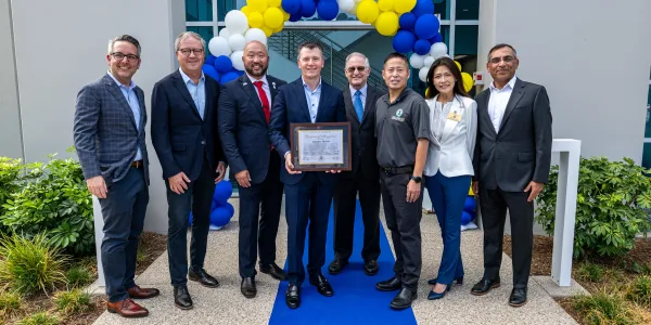 Eight people from SpyGlass Pharma and the Irvine City Council stand in front of a blue and yellow balloon arch. One man holds a certificate