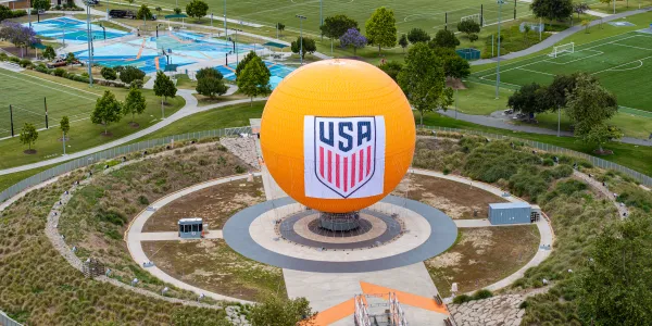 Large orange sphere with USA logo in a circular park, surrounded by green sports fields.