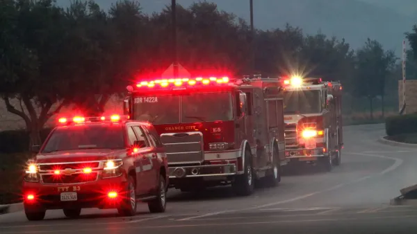 A line of fire trucks with flashing red lights on a road at dusk.