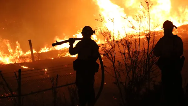 Silhouetted firefighters watching a raging wildfire at night.