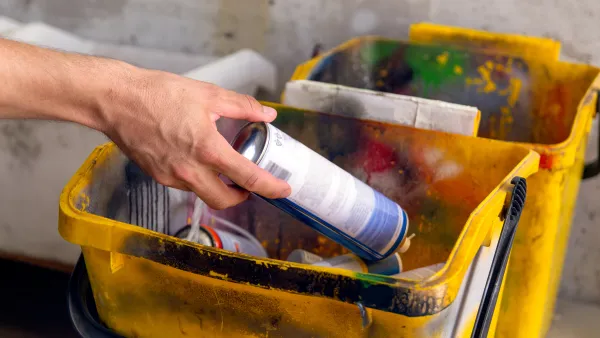 Hand places a spray paint can into a yellow, paint-splattered bucket.