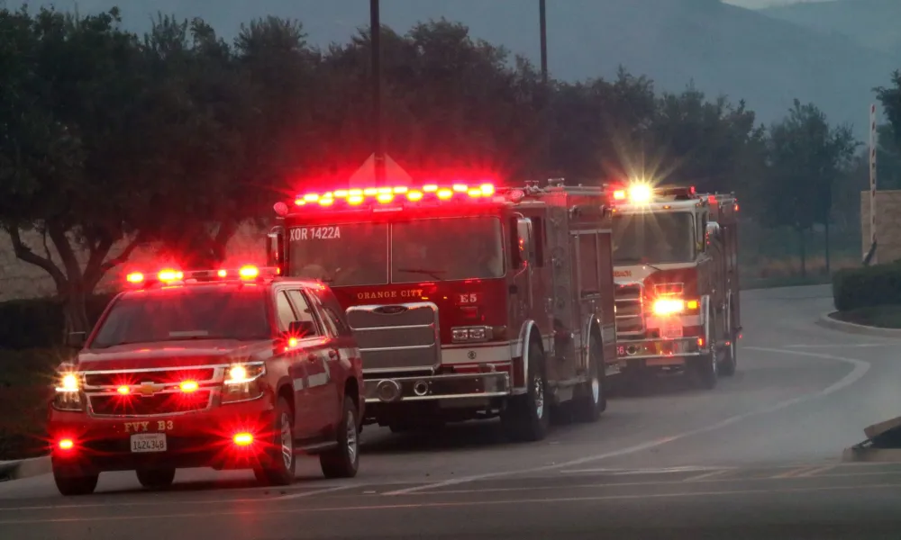 A line of fire trucks with flashing red lights on a road at dusk.