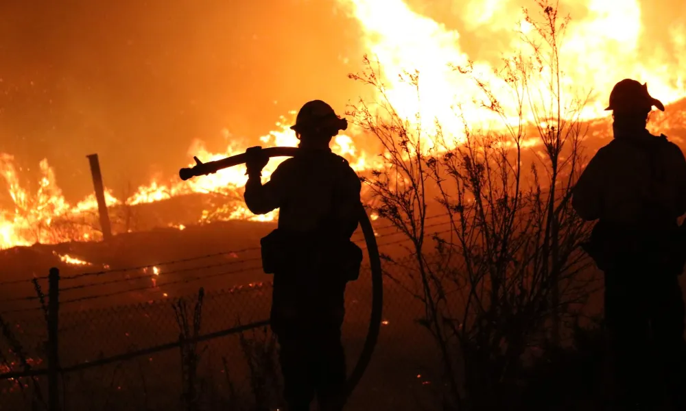 Silhouetted firefighters watching a raging wildfire at night.