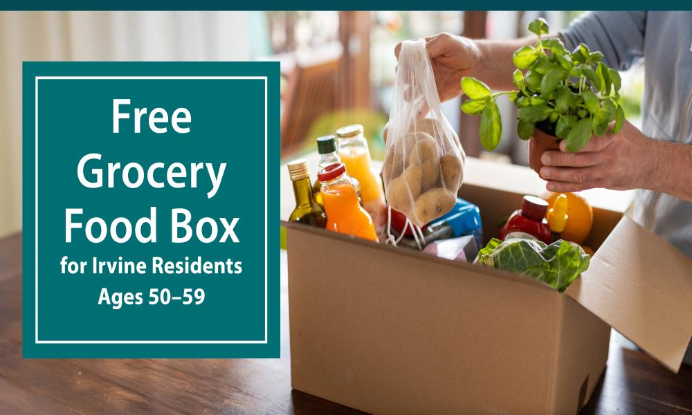 Person's hands filling a cardboard box with fresh groceries on a wooden table.