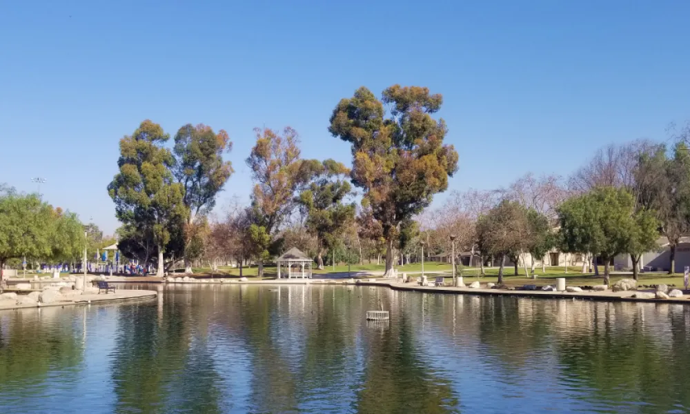 Sunny park with a reflective pond, many trees, and a white gazebo.