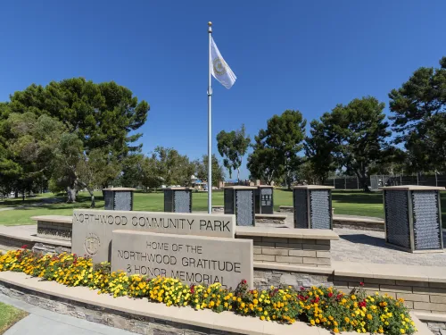 Northwood Community Park sign and war memorial with flag and flowers under a clear sky.