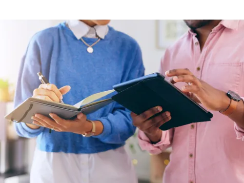 Two people talking holding an IPad and notebook