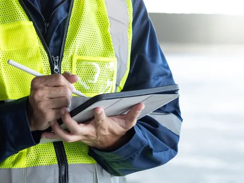 Worker in safety vest and uniform using a tablet with a stylus.