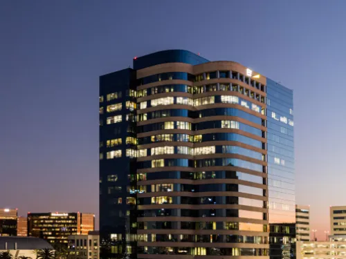Modern skyscraper with illuminated windows at dusk, part of a city skyline.