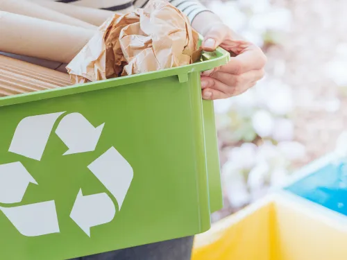 Person holding a green recycling bin full of cardboard and paper.