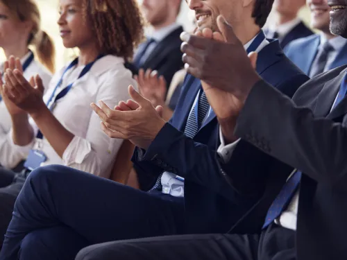 Audience of professionals clapping at a conference.