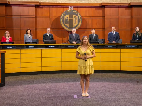 Seven member of City Council standing behind a young woman performing a song as an invocation in the Council Chamber