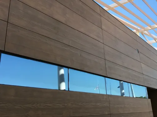 Modern building with dark brown panels, reflective blue windows, and a white structural roof.